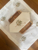 A rectangular placemat with embroidered forest trees on a white background, displayed on a wooden floor. pure linen