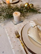 Elegant table setting with gold cutlery, white plates, and a candle on a decorative tablecloth.