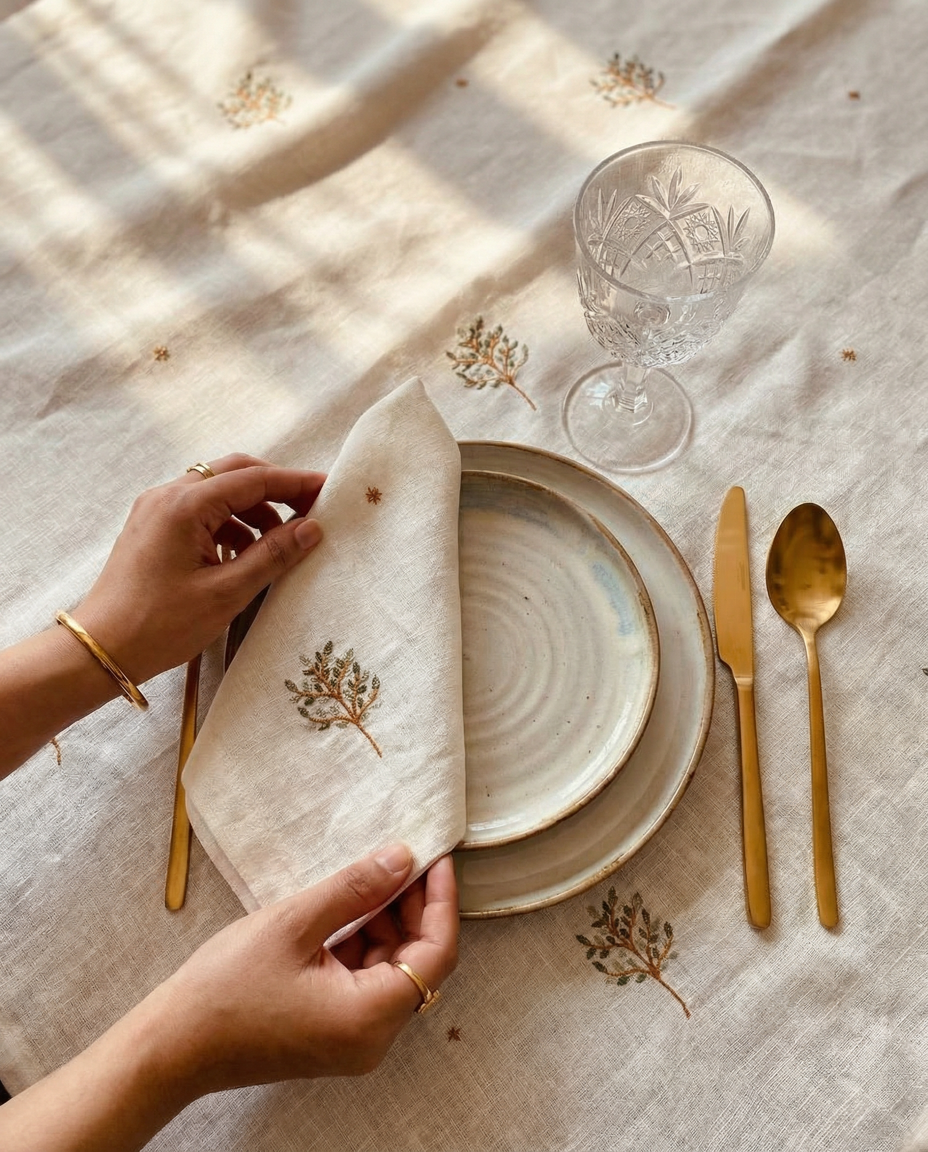 Person setting a table with a decorative napkin, plates, and cutlery on a textured surface. linen table napkin