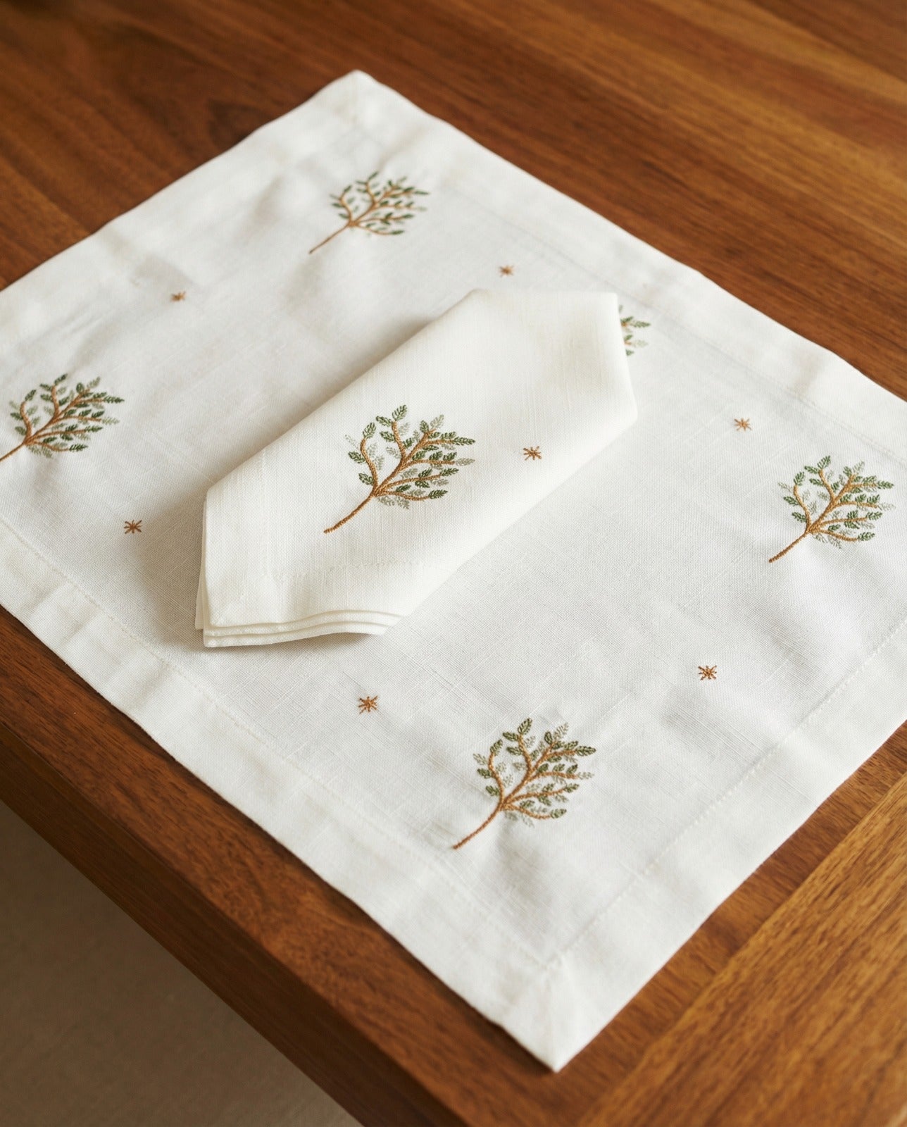 Set of white napkins with embroidered designs on a wooden surface