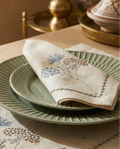 Decorative table setting with embroidered placemat, green plates, and embroidered napkin.