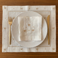 Elegant table setting with white plates, gold cutlery, and embroidered placemat on a wooden surface.