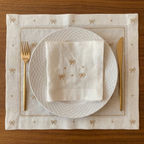 Elegant table setting with white plates, gold cutlery, and embroidered placemat on a wooden surface.