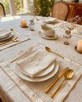 Elegant table setting with gold utensils, white plates, and candles on a light-PURE LINEN tablecloth.