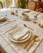 Elegant table setting with gold utensils, white plates, and candles on a light-PURE LINEN tablecloth.